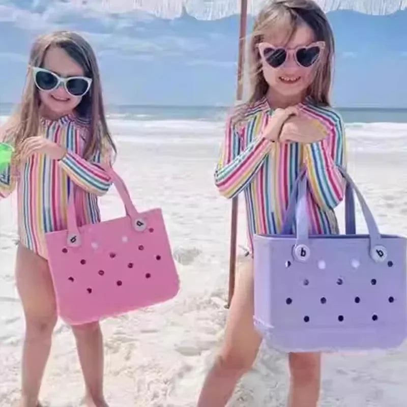 Two children on a beach wearing colorful outfits and holding beach bags.